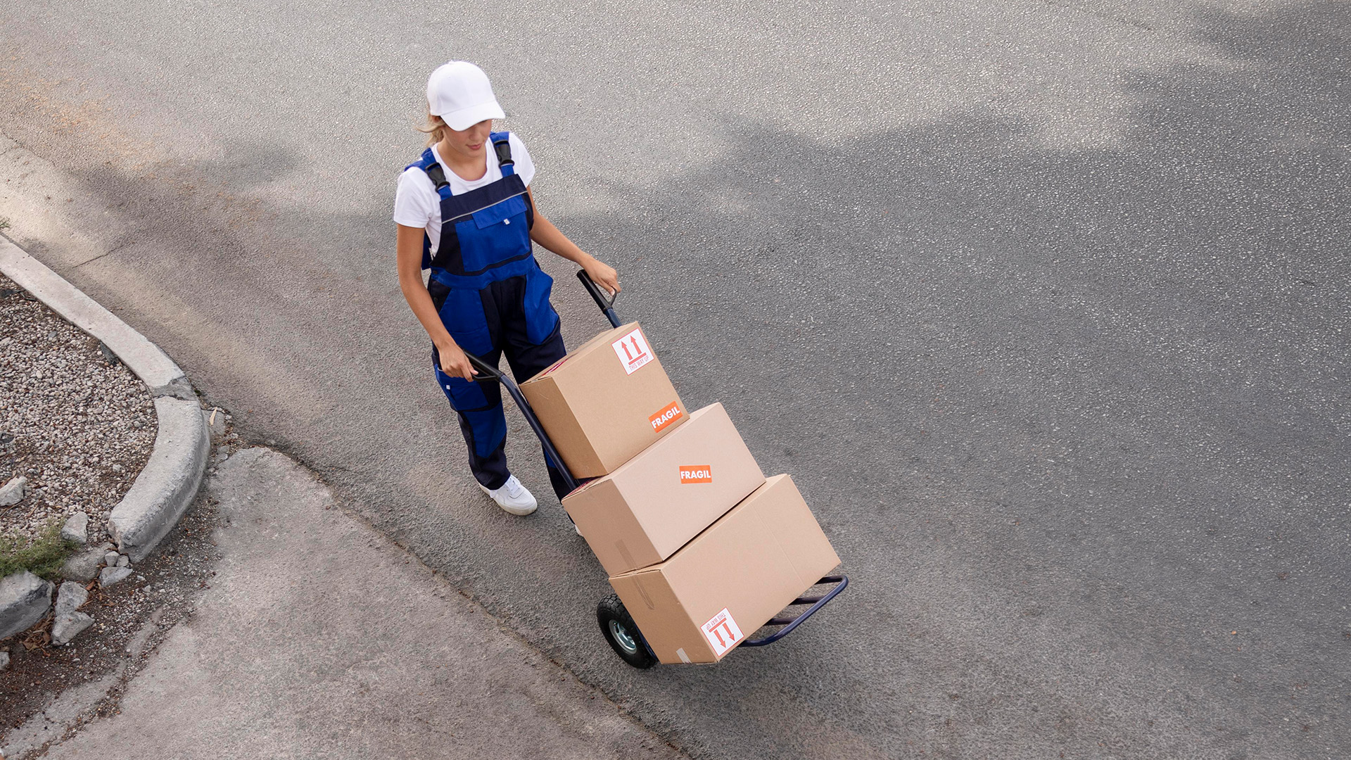 En tjej med vit keps och blå hängselbyxor drar kartonger på en pirra.